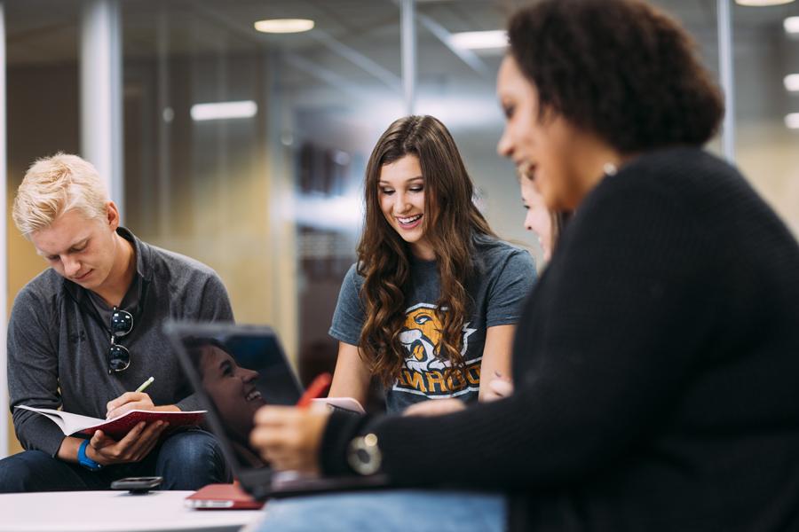 Doane studetns smiling while writing in a journal, reading from a book, and looking at their phone respectively.